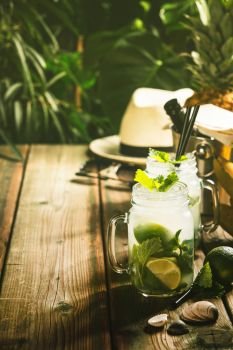 Summer vacation concept: white hat, drinks and tropical fruits on tropical leaves background. Summer vacation concept - against rustic tropical background