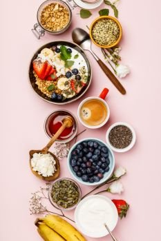 Healthy breakfast set. Oat granola with fresh berries, banana, yogurt, maple syrup, seeds and mint leaves  with cup of coffee on pink background, flat lay, top view