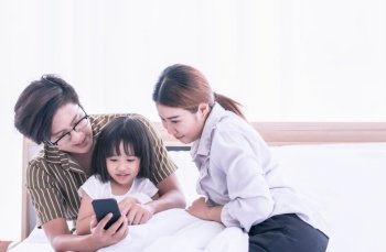 Asian parents helping their daughter to learn online at home via mobile phone