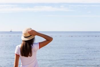 Beautiful girl looks at the sea. Young girl in a hat looking at a calm sea and blue skies back view.. Beautiful girl looks at the sea. Young girl in a hat