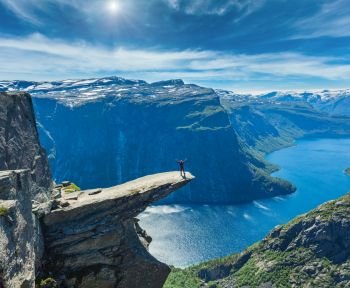 The summer sunshiny view of Trolltunga (famous The Troll’s tongue Norvegian destination) and Ringedalsvatnet lake in Odda, Roldal, Norway. Man tourist on rock.