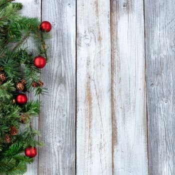 Christmas background with evergreen branches and red ornaments on white rustic wood 