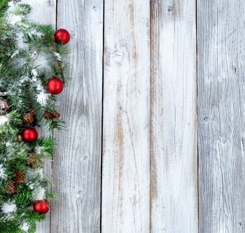 Christmas background with snow covered evergreen branches, gifts and red ornaments on white rustic wood 