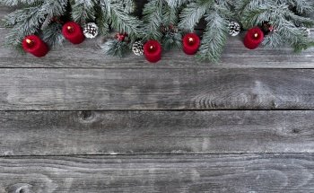 Snow covered evergreen branches with bright red burning candles, on faded wooden planks for a merry Christmas or happy New Year holiday celebration concept 