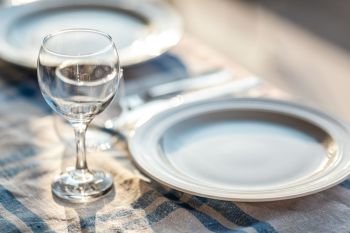 A fragment of a laid table with a tablecloth, a couple of plates, glasses and cutlery. Ready for dinner