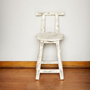 Rustic white wooden stool against a plain wall background