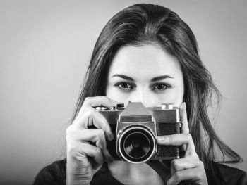 Photo of a beautiful woman pointing a vintage camera done in black and white.