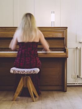 Photo of a blond woman in her early thirties playing the piano at home. Plenty of motion blur visible.