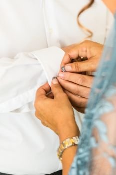 A groom putting on cuff-links as he gets dressed in his wedding day. A Groom’s suit