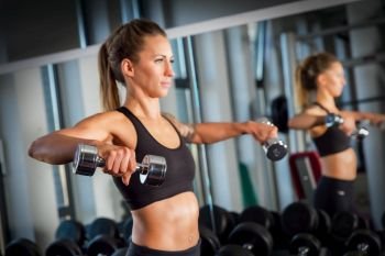 Young woman lifting dumbbells next to a mirror at a modern gym. Body training, weightlifting workout. Crossfit exercise.. Attractive woman weightlifting at the gym.