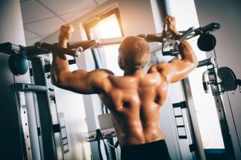 Muscular man exercising, using gym equipment. Bodybuilding. Heavy workout.. Strong man exercising in a gym.