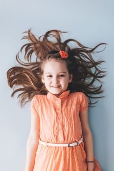 Young girl with messy hair laying down on the floor, smiling. Cheerful child.. Happy girl with messy hair laying down on the floor
