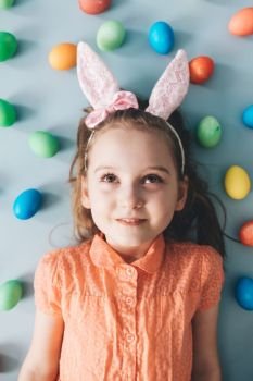 Cute young girl with pink bunny ears laying on the floor, surrounded by colorful eggs. Easter.. Girl with bunny ears surrounded by colorful eggs.