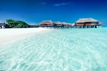 Fancy summer hotel with houses standing on stakes in the water. Clear blue water and beach on Maldives. Summer hotel with houses standing in the water on Maldives