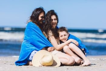 Mother and her children wrapped in a blanket, spending time by the sea. Summer break. Family holidays.. Mother and her children wrapped in a blanket by the sea.