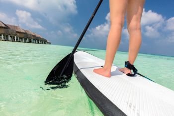 Woman does stand up paddle boarding on the ocean in Maldives. Light water sport on vacation. Woman does stand up paddle boarding on the ocean in Maldives