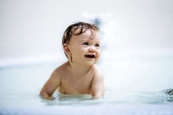 Little girl sitting in a shallow pool, laughing. Toddler. Playing in the water.. Laughing girl sitting in a shallow pool