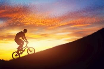 Man riding a bmx bike uphill against sunset sky. Active lifestyle, motivation, strength, challenge