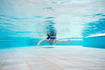 Young boy swimming underwater with swimming goggles on. Water park. Leisure activities.. Young boy swimming underwater