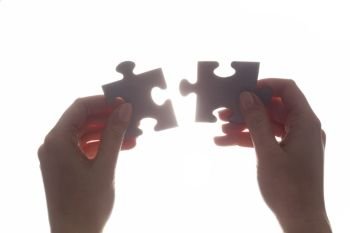 Joining two pieces of jigsaw puzzle. Backlit, isolated on white. Search for the solution, solving the problem, answer, business connection concept.