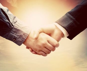 Business people shaking hands against sunny sky background in vintage mood. Conceptual handshake