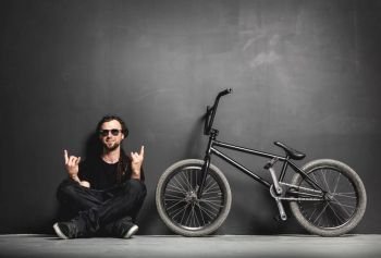 Happy man sitting next to his BMX bike, showing rocker gesture. Chill and relax.. Happy man sitting next to his BMX bike, showing rocker gesture.