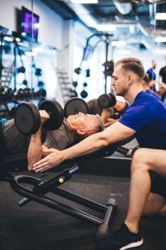 Young man assisting senior man at the gym. Personal trainer, retirement activities.. Young man assisting senior man at the gym.