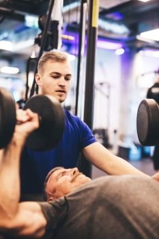 Personal trainer instructing older man during exercise. Gym activities. Weightlifting.. Personal trainer instructing older man during exercise.