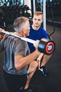 Personal trainer and senior man exercising at the gym. Gym assistant. Weightlifting.. Personal trainer and senior man exercising at the gym.