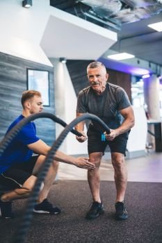 Senior man exercising with ropes at the gym. Personal training. Healthy lifestyle.. Senior man exercising with ropes at the gym.