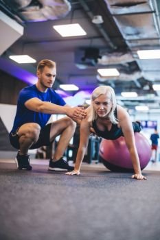 Woman exercising on a ball and a man securing her. Fitness coach. Gym activities.. Woman exercising on a ball and a man securing her.