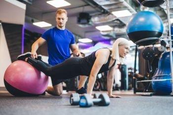 Woman working out on a ball with personal trainer. Gym instructor. Exercising.. Woman working out on a ball with personal trainer.
