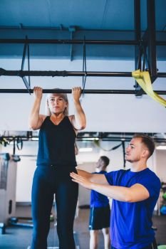 Woman doing pull-ups and a man securing her. Personal trainer. Workout assistance.. Woman doing pull-ups and a man securing her.