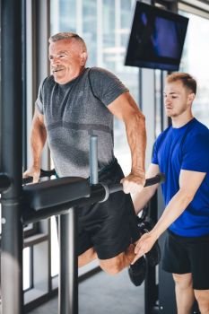 Gym instructor helping senior man at the gym. Sport and physical training.. Gym instructor helping senior man at the gym.