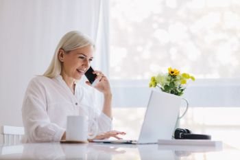 Woman talking on the phone, using laptop. Working from home, freelancing, online job.. Woman talking on the phone, using laptop.
