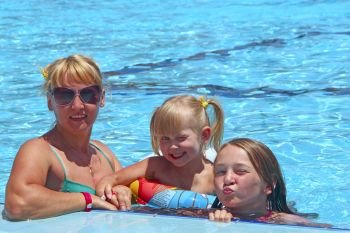 Happy mother with her daughters sitting in swimming pool posing in front of camera. Happy family team. Family enjoying summer vacations. People enjoying family holiday. Female team. Happy mother with her daughters sitting in swimming pool posing in front of camera