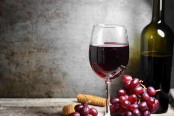 Glass of red wine on a wooden table in a rustic and vintage wine bar with grapes and a bottle of wine on background with copy space.