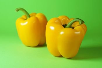 Peppers portrait concept with two yellow sweet bell peppers close up view on green background.