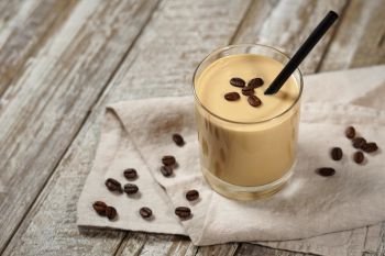 Cold coffee cream milkshake smoothie drink in a glass topped with coffee beans on a wooden rustic table with copy space.