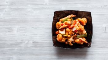 korean cuisine - top view of stir-fried Shrimps with cashew nuts and vegetables in sweet and sour sauce (Shrimps Combo) in black bowl on wooden board with copyspace