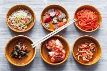 korean cuisine - chopsticks on bowls with various side dishes (Banchan or Panchan) on gray table