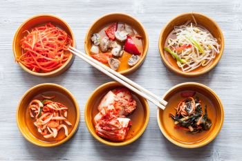 korean cuisine - chopsticks above various appetizers (Banchan or Panchan) in ceramic bowls on gray table