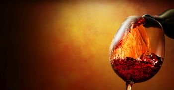 Wineglass with wine pouring from bottle on orange background