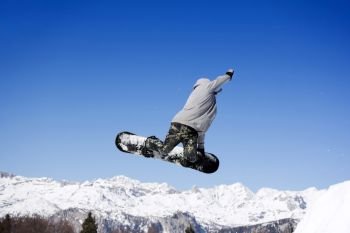Extreme Jumping Snowboarder at jump above mountains at sunny day
