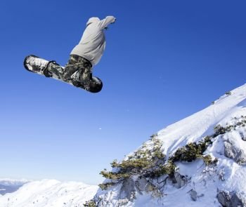 Extreme Jumping Snowboarder at jump above mountains at sunny day