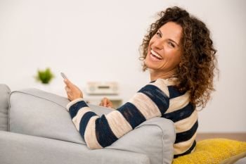 Beautiful woman sitting on the sofa and laughing while sending a text message