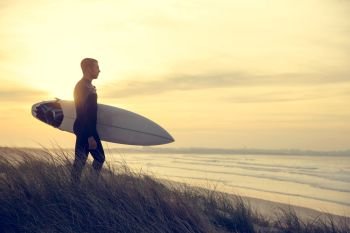 A surfer with his surfboard at the dunes looking to the waves