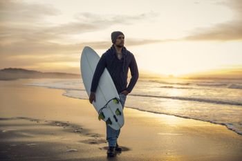 A surfer with his surfboard walking in the beach at the sunset