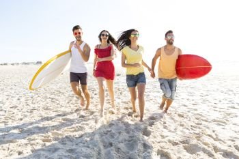 Group of friends walking together at the beach and holding surfboards