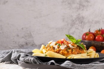 Tasty appetizing classic italian penne pasta with vegetarian lentil bolognese sauce, cheese parmesan and basil on plate on light table. Healthy eating concept.